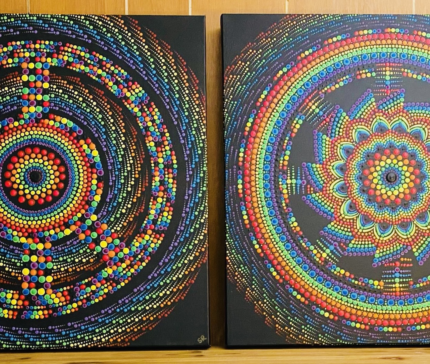 Two intricate paint mandalas, shown side by side on a wooden surface.