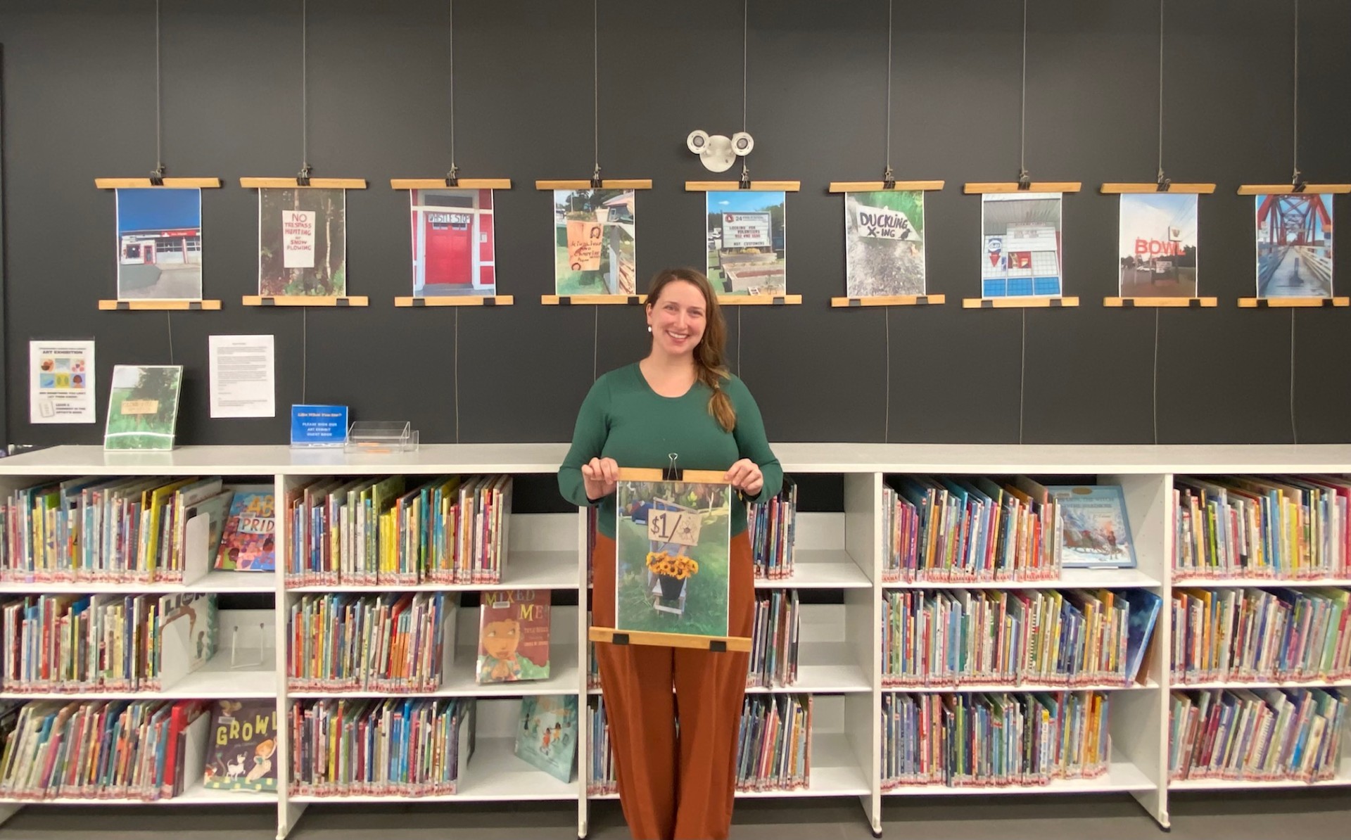 Artist Swanie Jahn Foley stands happily in front of their art display, at Musquodoboit Harbour Public Library.