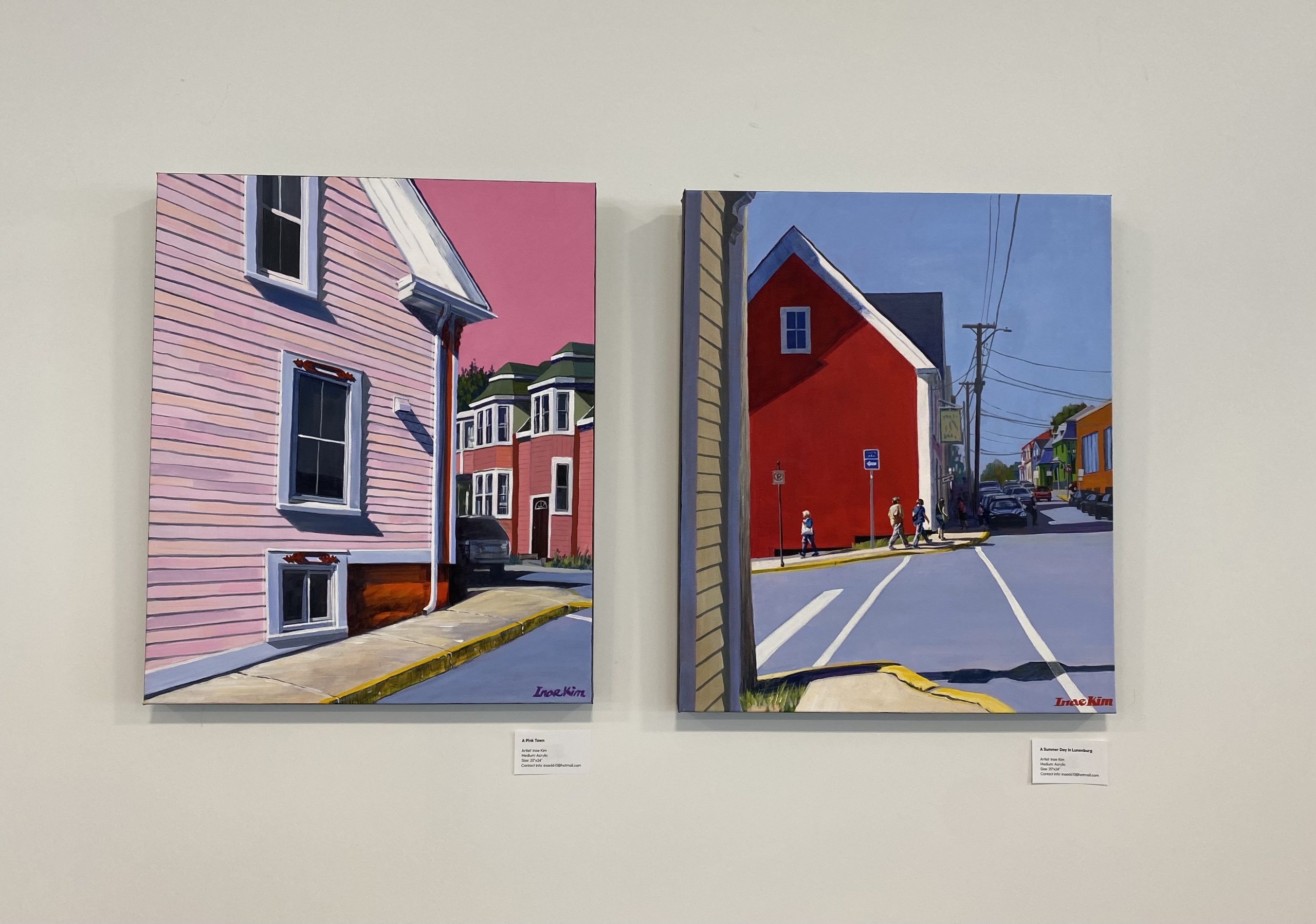 Two vibrant paintings of colourful houses appear side by side, set against a plain white wall.